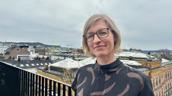 Portrett av lyshåret kvinne med briller med bylandskap i bakgrunnen