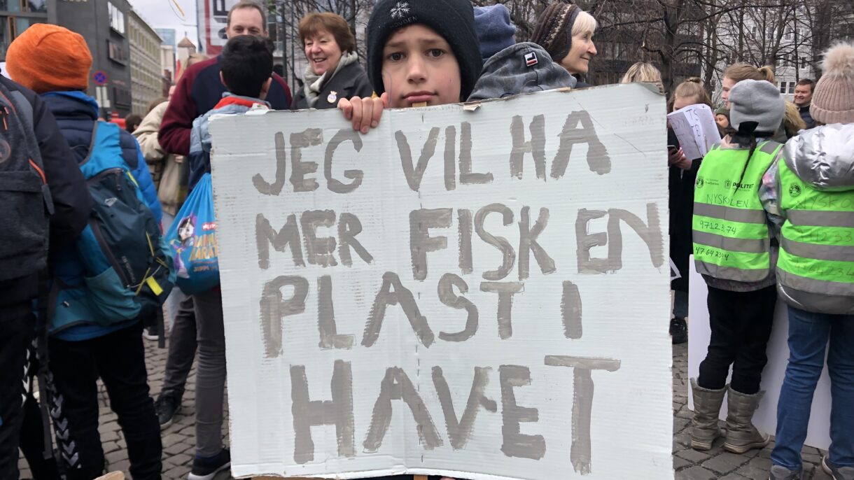 Gutt holder opp plakat hvor det står "Jeg vil ha mer fisk en plast i havet". Foto