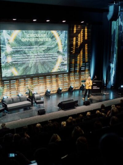 Konferanse med kvinne kledd i gul dressjakke på scenen. I bakgrunnen slide med teksten Circular Oppurtunites. Foto.