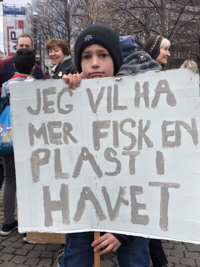 Gutt holder opp plakat hvor det står "Jeg vil ha mer fisk en plast i havet". Foto