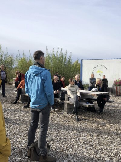 En gruppe mennesker får omvisning utendørs. Noen sitter og noen står. Foto.