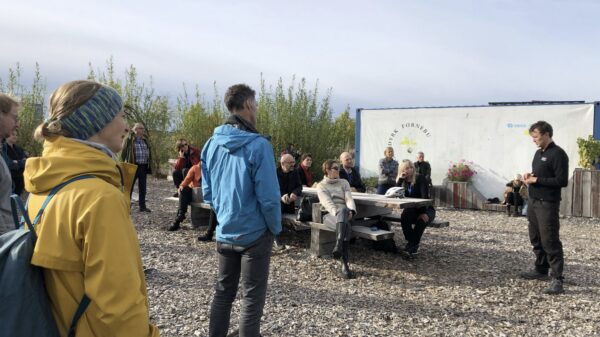 En gruppe mennesker får omvisning utendørs. Noen sitter og noen står. Foto.