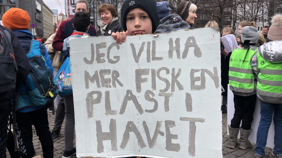 Gutt holder opp plakat hvor det står "Jeg vil ha mer fisk en plast i havet". Foto