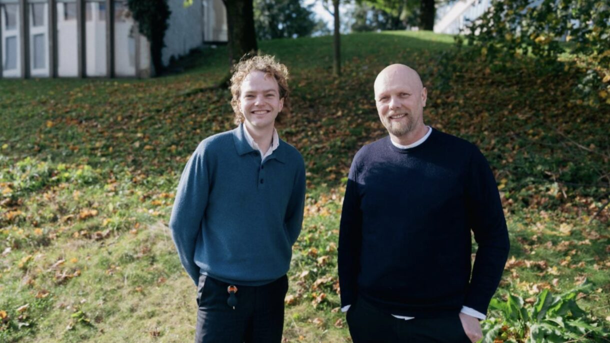 To smilende menn fotografert utendørs. Foto.