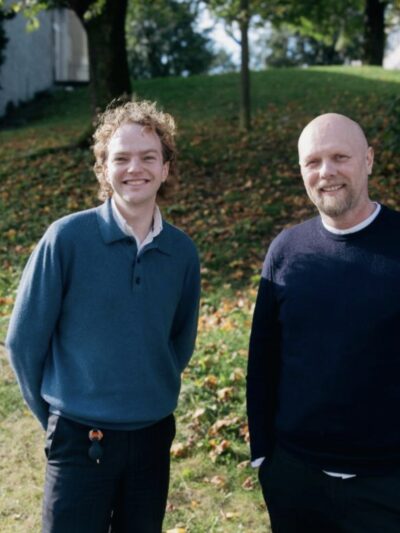 To smilende menn fotografert utendørs. Foto.