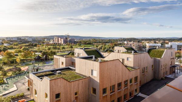 Klynge av bygg med fasader av tre og takhager. Fornebuparken i bakgrunnen.