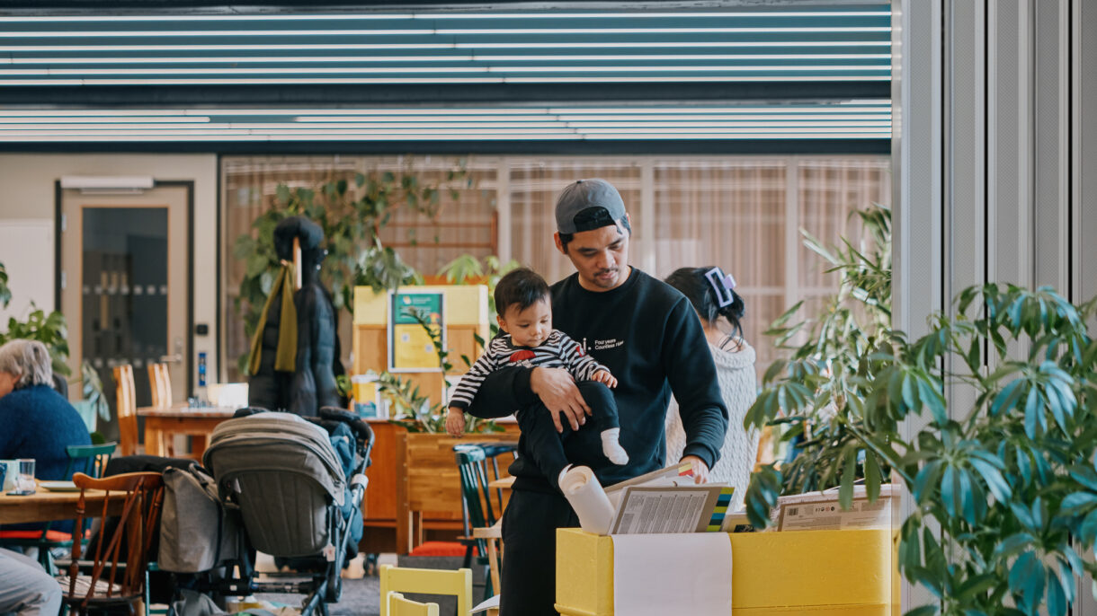 Mann holder baby i armene og ser på bøker. Foto.