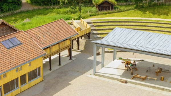 Trehus med rød takstein og plass med overbygg ved større plass. Foto.