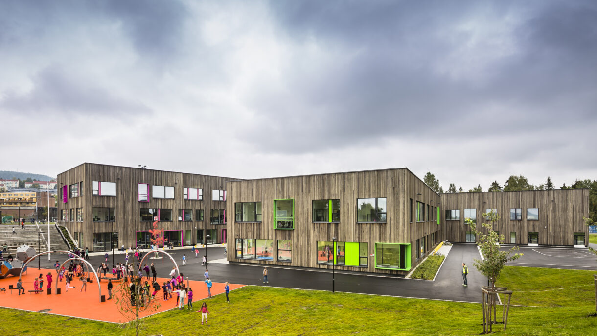 Skolegård. Skolebygg. Plen. Lekeapparat og barn. Foto