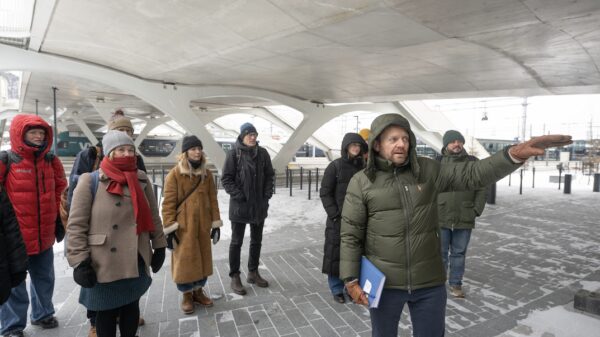 Mann peker og står foran en gruppe mennesker som er på omvisning. Foto.