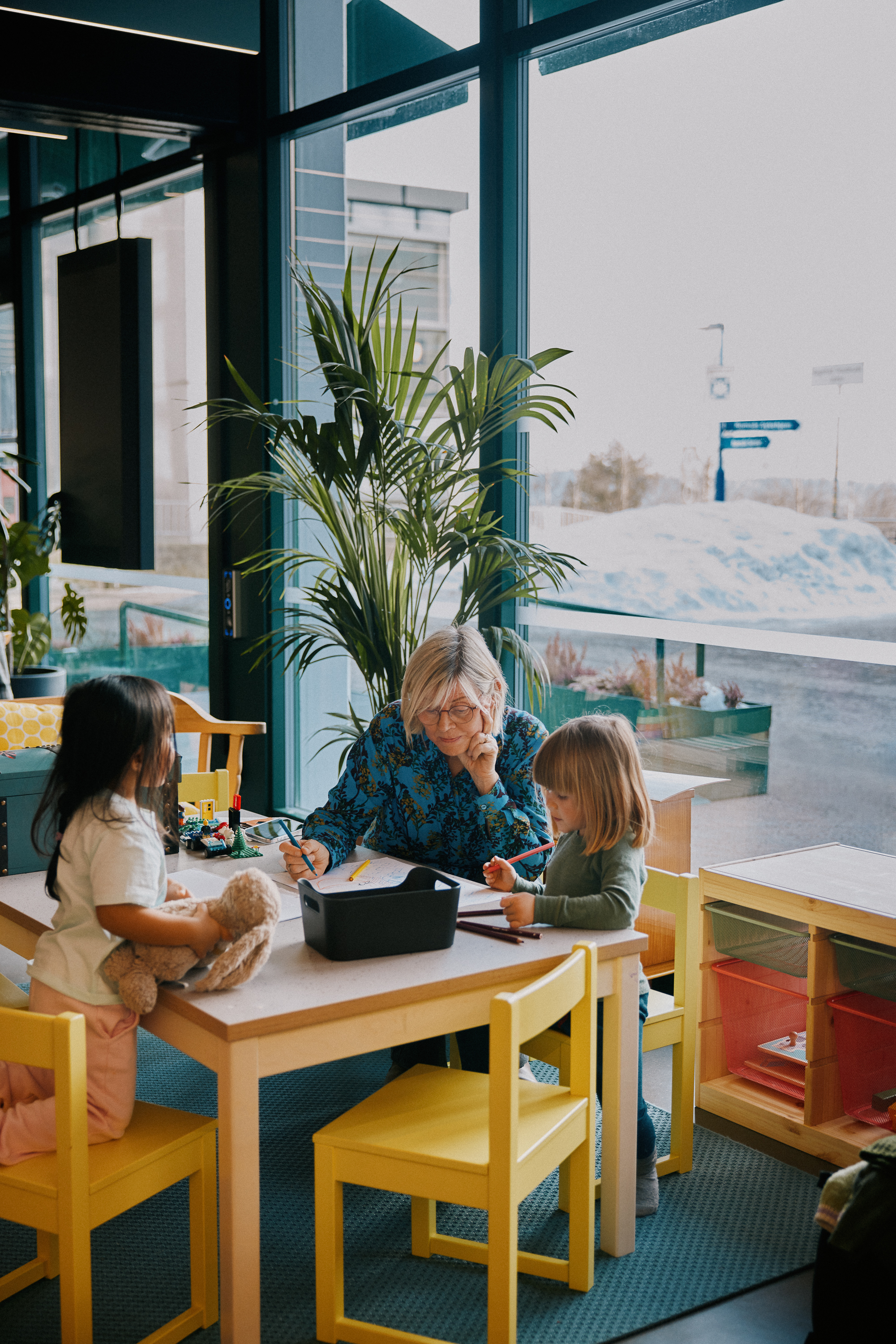 Kvinne og to barn som sitter og tegner. Foto.