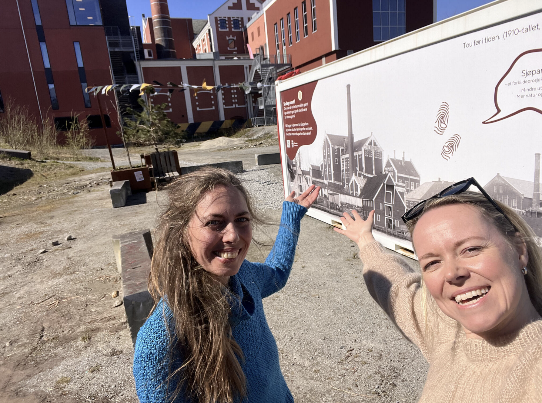 To kvinner peker mot en container som har et stort fotografi av gamle bygg på fasaden. Foto.